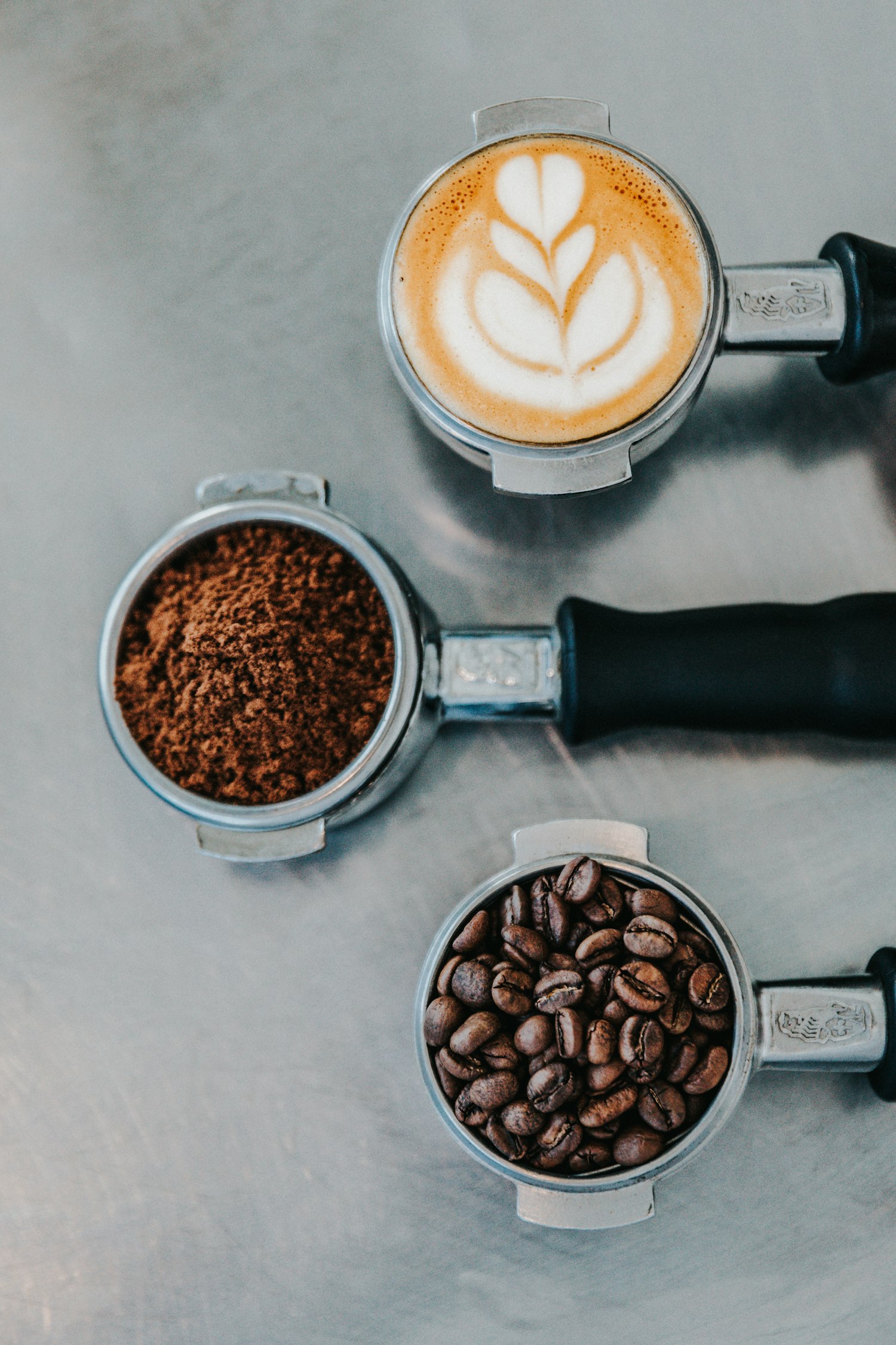 Drie portafilters met latte art, gemalen koffie en verse bonen